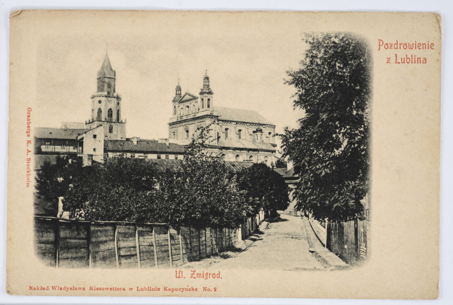 Pocztówka - ul. Żmigród w Lublinie (ujęcie w poziomie)
AWERS: Widok z ulicy Żmigród na zabudowania Katedry oraz Wieży Trynitarskiej. Na pierwszym planie wylot ulicy ogrodzonej po obu stronach drewnianym parkanem. Dalej zadrzewione podwórka kamienic przy ulicy Królewskiej. Zdjęcie, o wycieniowanych krawędziach, na białym polu. Wokół fotografii rozmieszczone napisy (w kolorze czerwonym) z tytułem pocztówki, nazwą wydawcy i numerem serii wydawniczej. W p.d. rogu zdjęcia na biało numer negatywu (?): 38376.
REWERS: Czarna linatura. U góry i u dołu nadruki informacyjne w języku rosyjskim i francuskim. W p.g. rogu miejsce na znaczek. Brak korespondencji oraz śladów obiegu pocztowego.

