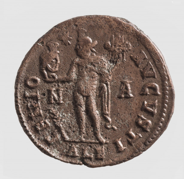 AV. Głowa cesarza w podwójnym wieńcu laurowym w profilu w prawo. W otoku napis:
FL VAER CONSTANTINVS P F AVG

RV. Stojący Geniusz w lewo. W jego rekach głowa Serapisa i róg obfitości. Litery: N  -  A
W otoku:
GENIO - AVGVSTI
Na dole w odcinku litery: ALE