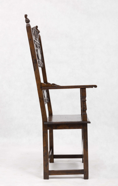 Fotel drewniany z  siedziskiem i oparciem drewnianym bez wyściełania, na prostych nogach z czterema łączynami. Nogi tylne przechodzą w ramiaki boczne oparcia. Oparcie prostokątne, lekko odchylone do tyłu. Zaplecek ażurowy złożony z dwóch bogato rzeźbionych desek:
- górna w ornamenty wolutowe wokół środkowago owalnego medalionu, z ozdobnie wyciątą dolną krawędzią i wyodrębnionym zwieńczeniem w kształcie przełamanego tympanonu z centralnym kartuszem
- dolna - węższa, powtarza główny motyw zdobienia.
Poręcze graniaste zakończone małymi wolutkami, u nasady rzeźbione liście akantu, podpórki w środkowej części rzeźbione. Płyta siedzenia prostokątna z rzeźbionym fartuchem z przodu. Łączyny boczne i tylna - graniaste, łączyna przednia w postaci deski o ozdobnym wykroju, rzeźbionej w ornamenty wolutowe.