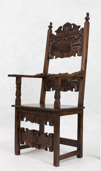 Fotel drewniany z  siedziskiem i oparciem drewnianym bez wyściełania, na prostych nogach z czterema łączynami. Nogi tylne przechodzą w ramiaki boczne oparcia. Oparcie prostokątne, lekko odchylone do tyłu. Zaplecek ażurowy złożony z dwóch bogato rzeźbionych desek:
- górna w ornamenty wolutowe wokół środkowago owalnego medalionu, z ozdobnie wyciątą dolną krawędzią i wyodrębnionym zwieńczeniem w kształcie przełamanego tympanonu z centralnym kartuszem
- dolna - węższa, powtarza główny motyw zdobienia.
Poręcze graniaste zakończone małymi wolutkami, u nasady rzeźbione liście akantu, podpórki w środkowej części rzeźbione. Płyta siedzenia prostokątna z rzeźbionym fartuchem z przodu. Łączyny boczne i tylna - graniaste, łączyna przednia w postaci deski o ozdobnym wykroju, rzeźbionej w ornamenty wolutowe.