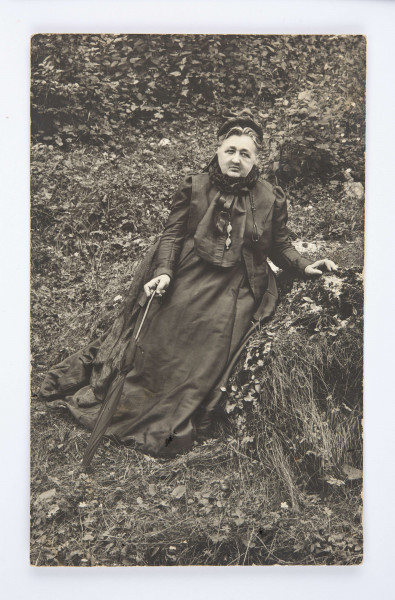 Oktawia Radziwiłłowicz siedząca na trawie. W dłoni trzyma parasolkę. Zawieszone na sznurku binokle.