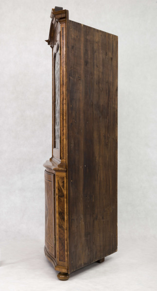 Szafa dwukondygnacyjna, z falistym zwieńczeniem, na nóżkach w kształcie spłaszczonych kul, wnętrze na planie trójkąta z półkami o falistych frontach. W części dolnej drzwi o wypukłym profilu zdobione fornirowanym wzorem: w centrum romb z przedstawieniem ptaka na gałęzi, wokół wzór szachownicy, krawędzie ujęte w ramę. W części górnej drzwi o falistym zwieńczeniu  oszklone szybkami łączonymi ołowiem.  
Oryginalny jest tylko front - pochodzący być może z szafy ściennej - całe wnętrze wykonano w XX wieku.  
