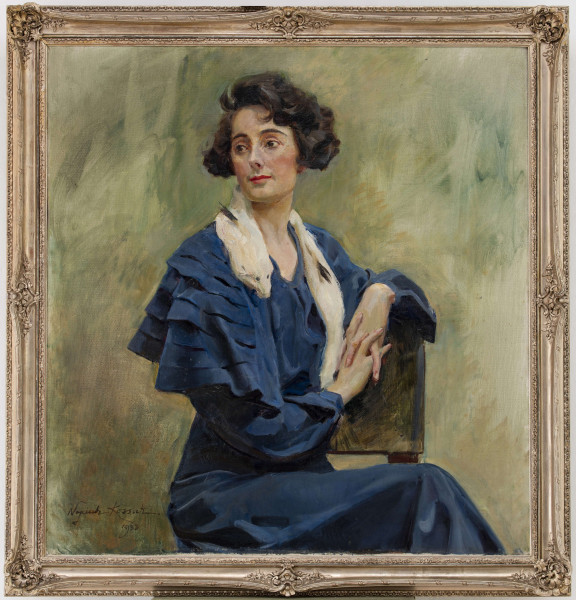 Portret kobiety w ujęciu do kolan. Siedzi bokiem, lekko zwrócona w prawą stronę. Twarz zwrócona w 3/4 w lewo. Lewa ręka wsparta na poręczy krzesła. Dłonie o szczupłych palcach, splecione. Kobieta jest ubrana w jedwabną, szafirową suknię z długimi rękawami i pelerynką złożoną z falban. Na szyi przerzucony biały lisek. Twarz szczupła, włosy, ułożone w fale, przykrywają uszy. Brwi zarysowane wyraźnym łukiem, oczy duże, nos prosty, lekko zadarty, wyraźnie zarysowane usta. Jednolite, zielonoszare tło. 