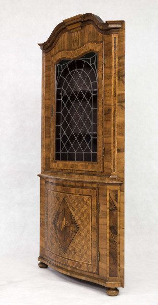 Szafa dwukondygnacyjna, z falistym zwieńczeniem, na nóżkach w kształcie spłaszczonych kul, wnętrze na planie trójkąta z półkami o falistych frontach. W części dolnej drzwi o wypukłym profilu zdobione fornirowanym wzorem: w centrum romb z przedstawieniem ptaka na gałęzi, wokół wzór szachownicy, krawędzie ujęte w ramę. W części górnej drzwi o falistym zwieńczeniu  oszklone szybkami łączonymi ołowiem.  
Oryginalny jest tylko front - pochodzący być może z szafy ściennej - całe wnętrze wykonano w XX wieku.  
