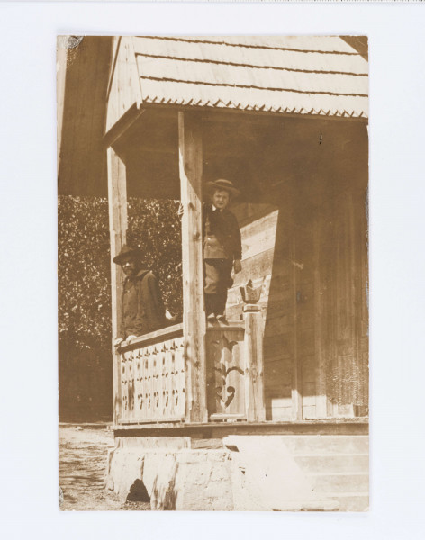 Stefan Żeromski z Adasiem na ganku Chaty w Nałęczowie. Adaś w kapeluszu stoi na balustradzie. 