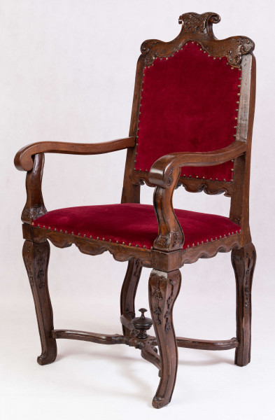 Fotel z tapicerowanym siedziskiem i oparciem, na czterech nogach wygiętych kabriolowo, połączonych skrzyżowanymi trawersami. Oskrzynienie prostokątne z fartuchem wysiętym w zęby przypominające lambrekin. Oparcie ażurowe, prostokątne, od góry zamknięte faliście z wolutowym szczytem pośrodku, deska dolna wycięta analogicznie do fartucha oskrzyni. Poręcze drewniane wyrastają z ramiaków bocznych oparcia, lekko wygięte, zakończone wolutami. Podpórki poręczy profilowane i rzeźbione w dolnej części.podobnie opracowanwe nogi, rzeźbione w liscie akantu u nasady, połączone wolutowymi trawersami z okrągłą sterczynką na skrzyżowaniu. Tapicerka na pasach, pokrycie bordowym aksamitem, na brzegach mosiężne gwoździe






  