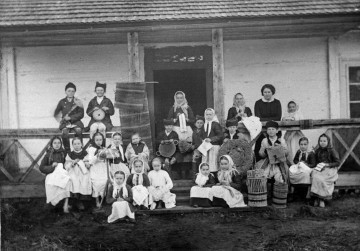 Fotografia czarno-biała przedstawia grupę osób - głównie dzieci - uczących się plecionkarstwa.