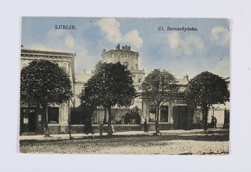 Pocztówka barwna z widokiem dawnego Pałacu Sobieskich przy ul. Bernardyńskiej w Lublinie. AWERS: Na pierwszym planie brukowana ulica, chodnik z kilkoma przechodniami oraz cztery drzewka liściaste z koroną przyciętą do kształtu zbliżonego do kuli. Po lewej stronie piętrowa kamienica. Na parterze sklep z szyldem z napisami w językach polskim i rosyjskim. Gmach pałacu zwieńczonego eklektyczną wieżą. Do ogrodzenia otaczającego pałac przylega parterowy budynek z dwoma oknami i drzwiami. Nad zabudowaniami niebieskie niebo z białymi chmurami i napisy z tytułem pocztówki. 
REWERS: Linatura w kolorze czarnym. Wyznaczone pole na korespondencję i adres. Pośrodku w pionie nadruk z informacją o wydawcy. Brak śladów obiegu pocztowego.