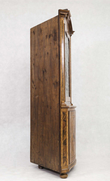 Szafa dwukondygnacyjna, z falistym zwieńczeniem, na nóżkach w kształcie spłaszczonych kul, wnętrze na planie trójkąta z półkami o falistych frontach. W części dolnej drzwi o wypukłym profilu zdobione fornirowanym wzorem: w centrum romb z przedstawieniem ptaka na gałęzi, wokół wzór szachownicy, krawędzie ujęte w ramę. W części górnej drzwi o falistym zwieńczeniu  oszklone szybkami łączonymi ołowiem.  
Oryginalny jest tylko front - pochodzący być może z szafy ściennej - całe wnętrze wykonano w XX wieku.  
