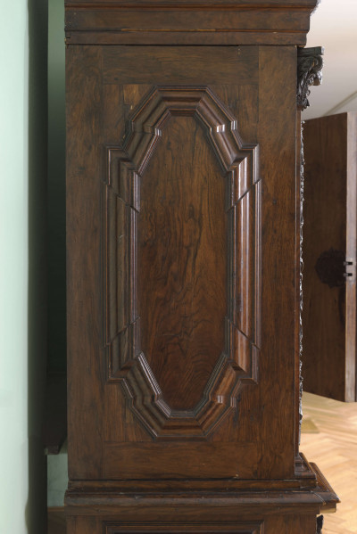 Korpus jednokondygnacyjny, na niskim cokole ze ślepą szufladą, zwieńczony rozbudowanym gzymsem wypiętrzonym i przełamanym pośrodku, dwoje drzwi z bogato profilowanymi płycinami, 5 nóg w kształcie spłaszczonych, fazowanych kul. Podział pionowy trzema pilastrami, z których środkowy jest listwą przymykową. Ich powierzchnie pokrywa wstęgowa snycerka z ornamentów roślinno-kwiatowych z wplecionymi puttami i ptakami, w głowicach rzeźbione główki. W załamaniu gzymsu przedstawienie Wenus z amorkiem na tle muszli otoczonej kwiatami, zwieńczonej koroną trzymaną przez dwa putta. We fryzie ornament roślinny z ptakami. W górnych narożach drzwi personifikacje Czterech Pór Roku.