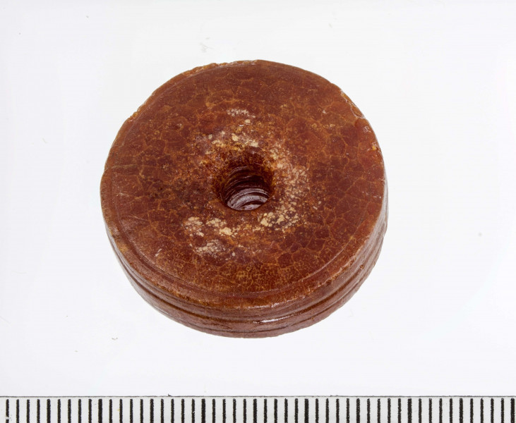 Paciorek typu II, tarczowaty, wypukły. Obie płaszczyzny paciorka zdobione pojedyńczymi liniami rytymi. Bok paciorka zdobiony parą dookolnych bruzd. Widoczne ślady toczenia.