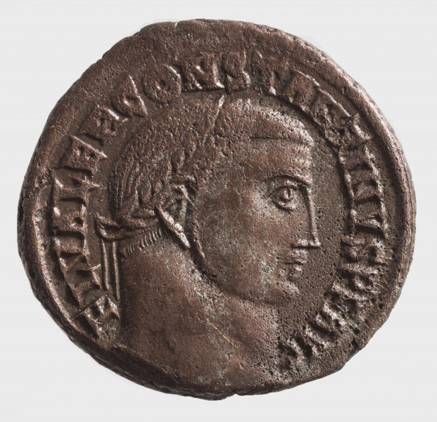 AV. Głowa cesarza w podwójnym wieńcu laurowym w profilu w prawo. W otoku napis:
FL VAER CONSTANTINVS P F AVG

RV. Stojący Geniusz w lewo. W jego rekach głowa Serapisa i róg obfitości. Litery: N  -  A
W otoku:
GENIO - AVGVSTI
Na dole w odcinku litery: ALE