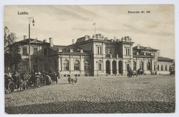 Pocztówka w sepii z widokiem zabudowań dworca kolejowego w Lublinie. 
AWERS: Na pierwszym wybrukowany planie plac dworcowy. Po lewej stronie i przed wejściem do dworca kilka oczekujących dorożek konnych. Fasada północna dworca w stylu neoklasycystycznym, przed przebudową w stylu modernistycznym. U góry napis drukiem z tytułem pocztówki. 
REWERS: Linatura w kolorze czarnym. Wyznaczone pole na korespondencję i adres. U góry drukiem napis informacyjny w językach francuskim, polskim i rosyjskim. Przy lewej krawędzi pola tekstowego nadruk z informacją o wydawcy. Przy dolnej krawędzi, pod miejscem na adres, napis z nazwą sprzedawcy (?). Brak śladów obiegu pocztowego.