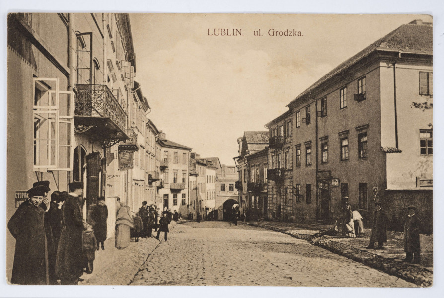 Pocztówka w sepii z widokiem ul. Grodzkiej na odcinku od placu po Farze do Bramy Grodzkiej. 
AWERS: Ulica z brukowanymi chodnikami i rynsztokami oraz ciągiem kamienic po obu stronach. Widoczne balkony z metalowymi balustradami. Kamienice po lewej stronie mają otwarte okna. N kilku z nich szyldy reklamowe. Na ulicy przechodnie, w tym ludność żydowska. Mężczyźni ubrani w ciemne płaszcze, kobiety z chustami na głowach. W lewym dolnym rogu młody mężczyzna ze zmrużonymi oczami zwrócony do widza. Wzdłuż górnej krawędzi pośrodku drukiem tytuł pocztówki. 
REWERS: Linatura w kolorze czarnym, wyznaczone pole na korespondencję, u góry nadruk w językach francuskim, polskim i rosyjskim. Pod polem tekstowym u dołu drukiem nazwa wydawcy. Brak śladów obiegu pocztowego.