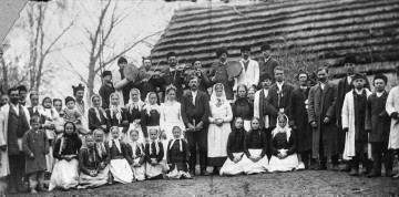 Fotografia czarno-biała wykonana podczas wesela. Przedstawia grupę ludzi i kapelę ludową ubranych w stroje ludowe.