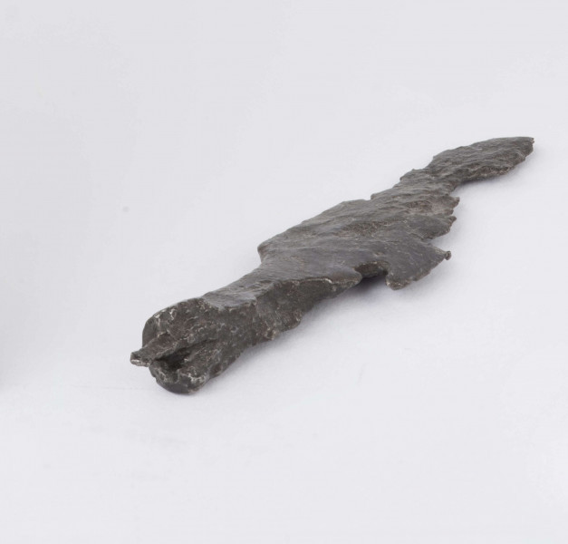 Żelazny grot strzały z wyraźnie wyodrębnionym od tulejki ostrzem; tulejka pełna, płasko sklepana w dolnej partii okrągła; zachowany mały fragment trzpienia