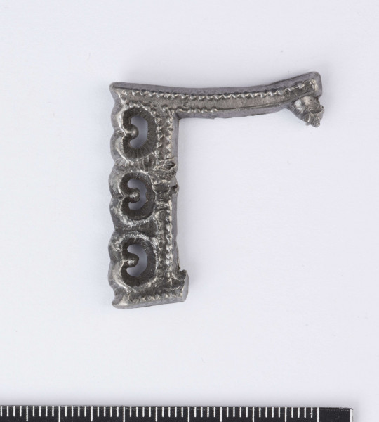 Sprzączka do pasa zachowana fragmentarycznie wykonana ze srebra, zdobiona . Ramka prostokątna. Przednia część ramki zdobiona trzema wypukłymi sercowatymi ornamentami z wyciętymi środkami w kształcie półksiężyca. Wszystkie wypukłości wyżej opisanego ornamentu oraz krawędzie sprzączki zdobione drobnym granulatem. Surowiec - srebro. Wymiary: średnia grubość 0,4; wymiary boków ramki 3,4 i 3,2 cm. Stan zachowania dobry. 