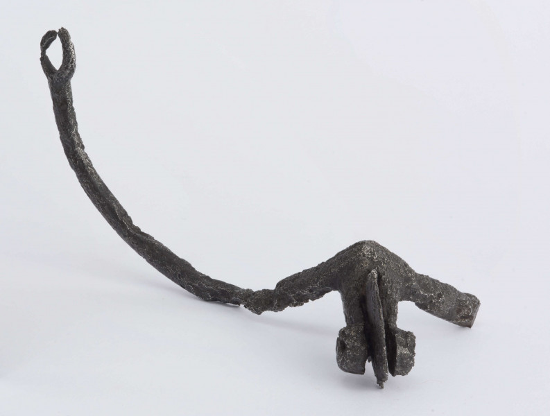 Ostroga żelazna - kabłąk w przekroju poprzecznym trójkątny zakończony kółkiem. Szyjka bodźca zwężająca się, na końcu w rozwidleniu przymocowana nitem gwiazdka (widełki z gwiazdką). Jedno ramie kabłąka uszkodzone, drugie w pobliżu nasady bodźca ułamane. Wymiary: długość ok. 11; rozpiętość kabłąka 10; szyjka dł. 3; średn. gwiazdki 2,5(zachowana); średnica kółka na końcu kabłąka 1,5 cm. Surowiec - żelazo. Stan zachowania - jedno ramię kabłąka uszkodzone, drugie w pobliżu bodźca ułamane. Zabiegi konserwatorskie - zakonserwowane (oczyszczone i zabezpieczone przed korozją).