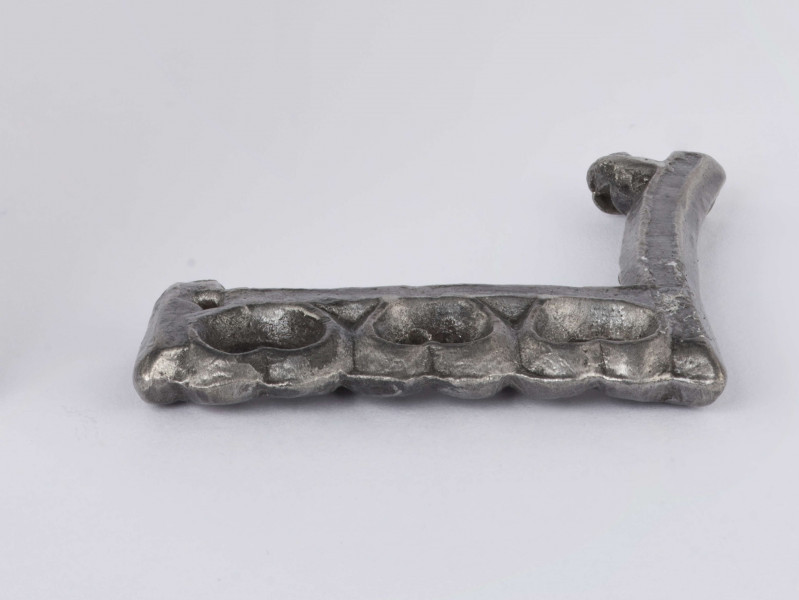 Sprzączka do pasa zachowana fragmentarycznie wykonana ze srebra, zdobiona . Ramka prostokątna. Przednia część ramki zdobiona trzema wypukłymi sercowatymi ornamentami z wyciętymi środkami w kształcie półksiężyca. Wszystkie wypukłości wyżej opisanego ornamentu oraz krawędzie sprzączki zdobione drobnym granulatem. Surowiec - srebro. Wymiary: średnia grubość 0,4; wymiary boków ramki 3,4 i 3,2 cm. Stan zachowania dobry. 