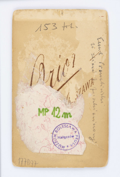 Fotografia portretowa Emila Trembińskiego. Chłopiec gładko uczesany, twarz skierowana w lewą stronę. Ubrany w ciemną koszulę z muszką pod brodą.  Pod fotografią znajduje się wydrukowany podpis: Orion Warszawa. Na odwrocie znajduje się przyklejony fragment białej kartki który zasłania wydrukowany napis. Z prawej strony widnieje napis wykonany ołówkiem: Emil Trembiński.