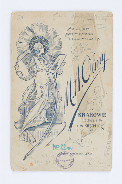 Fotografia przedstawia Julie Dąbrowską z Głoskowskich. Kobieta ubrana jest w biały, haftowany strój zapięty pod brodą przy pomocy broszki z jasnym kamieniem. Na szyi znajduje się długi łańcuszek, owinięty wokół szyi. Zdjęcie naklejone jest na firmową tekturę. W lewym, dolnym rogu znajduje się nazwa firmy która wykonała fotografię: M.A.Olma Kraków. W lewym dolnym rogu znajduje się napis: Krynica. Na odwrocie, wzdłuż lewej strony, znajduje się ilustracja przedstawiający kobietę, w długiej sukni z motywem kwiatowym, która w dłoniach trzyma lupę oraz fotografię z budynkiem, stojącą na tle kwiatu.  Po prawej stronie znajduje się drukowany napis z nazwą zakładu fotograficznego: „Zakład Artystyczno-fotograficzny M.A. Olmy w KRAKOWIE Podwale 14 i w Krynicy”.
