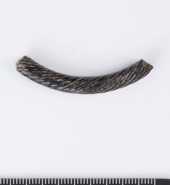 Fragment szklanej bransolety zdobionej kilkoma równolegle do siebie biegnącymi spiralnie wokół bransolety żłobkami. Bransoleta w przekroju okragła. Surowiec - szkło, barwa ciemno-brązowa. Wymiary: dł. 4,2; średn. 0,5 cm. Stan zachowania dobry.