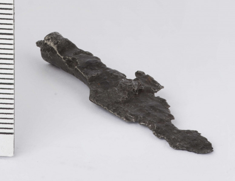 Żelazny grot strzały z wyraźnie wyodrębnionym od tulejki ostrzem; tulejka pełna, płasko sklepana w dolnej partii okrągła; zachowany mały fragment trzpienia