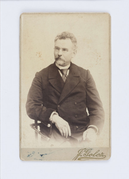 Fotografia przedstawia pisarza siedzącego na krześle. Ma krótkie włosy, na nosie znajdują się okrągłe okulary. Ubrany jest w dwuczęściowy, czarny garnitur, białą koszulę oraz ciemny krawat. Fotografia naklejona jest na tekturę firmową. W prawym, dolnym rogu znajduje się drukowany podpis fotografa: J. Golcz. Na odwrocie, w lewym, górnym rogu znajduje się drukowany napis: „FOTOGRAFJA TEATRÓW/ i towarzystwa/ Zachęty Sztuk Pięknych”. Niżej znajduje się odręczny napis wykonany flamastrem: „Bolesław Prus/ Przypuszcz. 11845 1900”. Po środku znajduje się nazwa firmy fotograficznej: „JADWIGA GOLCZ/ dawniej/ E. Troczewski i Ska”. W prawym, dolnym rogu znajduje się adres: Warszawa/ Erywańska.3.