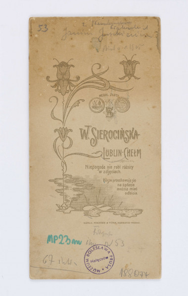 Fotografia przedstawia Janinę Juszkiewiczową z Głoskowskich. Ubrana jest w szarą koszulę, długą, ciemną spódnicę z czarnym paskiem, a pod szyją widać czarny kołnierzyk. Kobieta opiera się o drewniany stolik. W lewym, dolnym rogu znajduje się drukowany podpis autora zdjęcia: W. Sierocińska. W prawym dolnym rogu znajduje się napis: Chełm-Lublin. Na odwrocie znajduje się ilustracja z motywem kwiatowym. Obok znajduje się drukowany tekst: „W. Sierocińska/ Lublin-Chełm/ Niepogoda nie robi różnicy/ w zdjęciach/ Klisze przechowuje się/ na żądanie/ może mieć/ odbicia”.