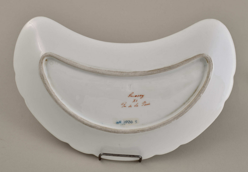 Talerzyk przystawkowy, w kształcie półksiężyca, z wyzębionym brzegiem, biały, z koroną hrabiowską. Spód