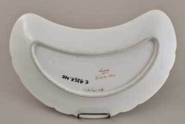 Talerzyk przystawkowy, w kształcie półksiężyca, z wyzębionym brzegiem, biały, z koroną hrabiowską. Spód