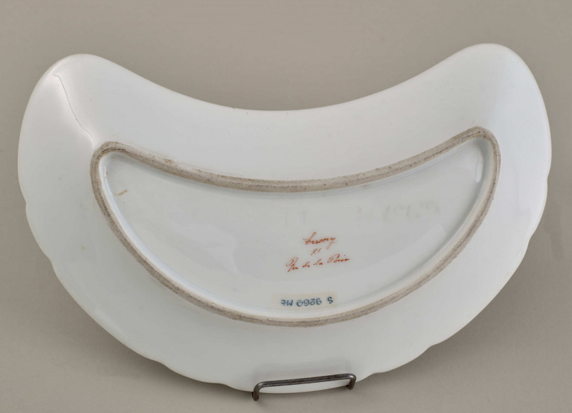 Talerzyk przystawkowy, w kształcie półksiężyca, z wyzębionym brzegiem, biały, z koroną hrabiowską. Spód