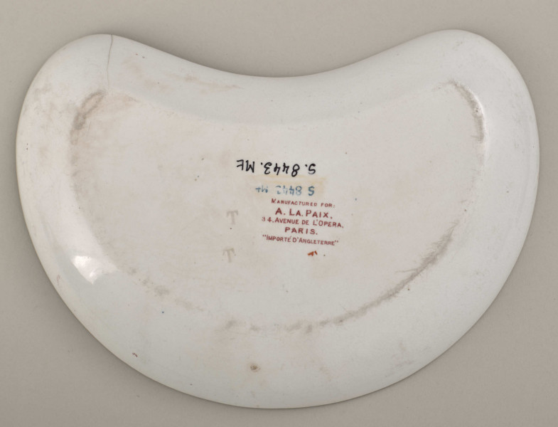 Talerzyk przystawkowy w krztałcie półksiężyca, zdobiony motywem roślinnym, kwiatowym i geometrycznym w kolorze czerwonym. Spód