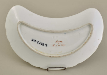 Talerzyk przystawkowy, w krztałcie półksiężyca, z wyzębionym brzegiem, biały,z koroną hrabiowską. Spód