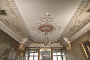 Pokój pod Orłami. Widoczny sufit z szaro-czerwonymi zdobieniami. Po bokach widoczne dwa orły otoczone zdobieniami o motywie roślinnym.