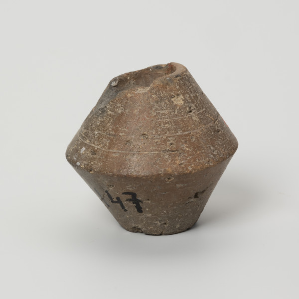 Przęślik dwustożkowy - ujęcie z boku; Przęślik gliniany dwustożkowy o ściętych, płaskich biegunach, dobrze wypalony, o barwie jasnobrązowej. Na powierzchni widoczne ślady toczenia oraz miejscami ubytki gliny. Wzdłuż osi pionowej przęślika znajduje się otwór o średnicy ok. 0,8 cm. Jeden z biegunów nieznacznie uszkodzony.