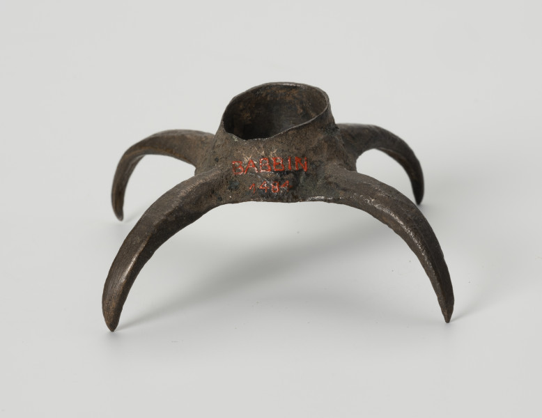 Pobocznica wędzidła końskiego (krępulec) - ujęcie z tyłu; Krępulec tzw. kolczasty złożony jest z niewielkiej tulejki zaopatrzonej w cztery kolczaste ramiona lekko zagięte do środka. Przedmiot wykonany jest z brązu.