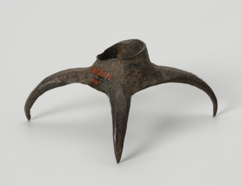 Pobocznica wędzidła końskiego (krępulec) - ujęcie z tyłu; Krępulec tzw. kolczasty złożony jest z niewielkiej tulejki zaopatrzonej w cztery kolczaste ramiona lekko zagięte do środka. Przedmiot wykonany jest z brązu.