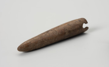 Igielnik - ujęcie z boku; Igielnik wykonany z naturalnego zakończenia poroża. Zdobiony delikatnymi rysami nie tworzącymi wyraźnego ornamentu. W górnej części znajdują się dwa uszkodzone naprzeciwległe okrągłe otwory do mocowania sznurka lub rzemyka.