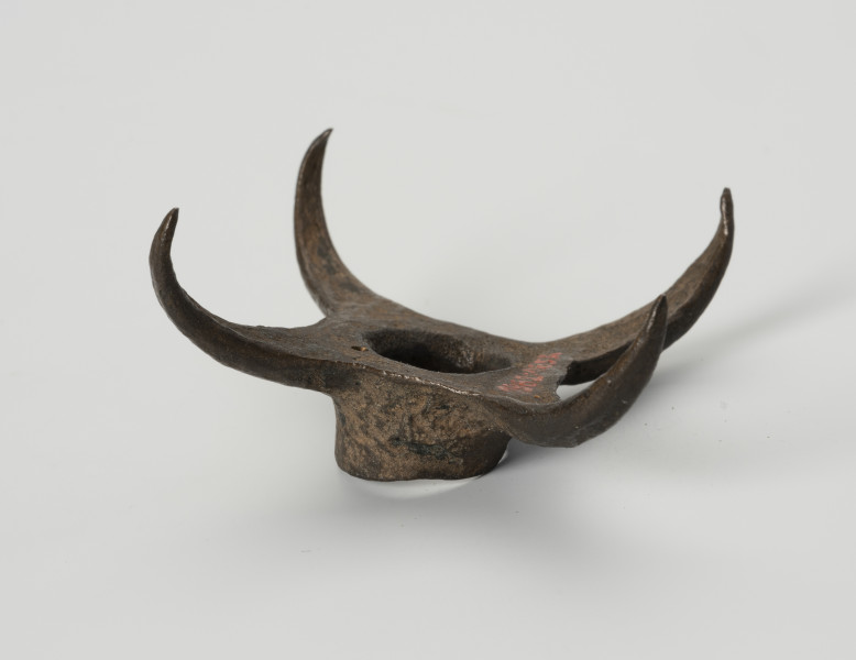 Pobocznica wędzidła końskiego (krępulec) - ujęcie z boku; Krępulec tzw. kolczasty złożony jest z niewielkiej tulejki zaopatrzonej w cztery kolczaste ramiona lekko zagięte do środka. Przedmiot wykonany jest z brązu.