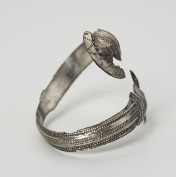 Bransoleta żmijowata - ujęcie z boku; Srebrna bransoleta żmijowata. Średnica zakończeń wynosi 2,8 – 2,9 cm. Obie główki (zakończenia) bransolety są zdobione puncą i filgranem oraz posiadają szerokie ornamentowane kryzy.