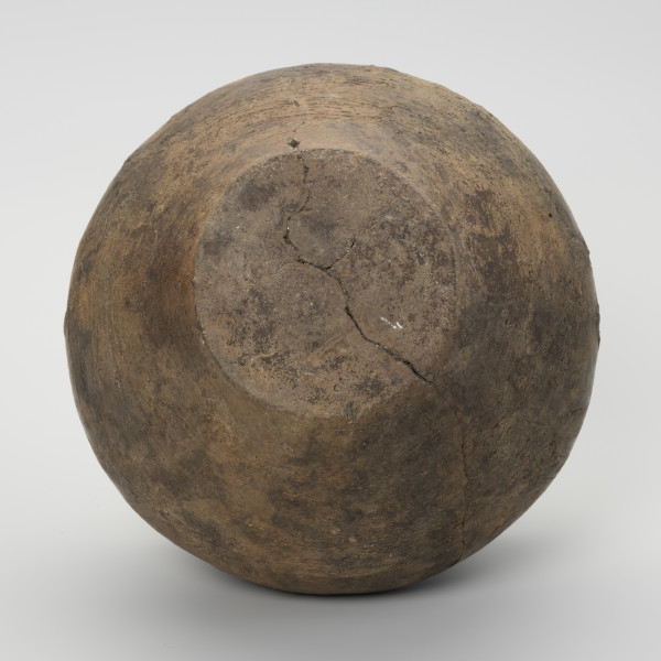 Waza typu IV (Wołągiewicz) - ujęcie z dołu; Naczynie ceramiczne (waza) barwy ciemno brunatnej o chropowaconej części dolnej i wygładzanej górnej partii. Waza ma dwa przewężone ucha. Na brzuścu zdobiona chropowaconymi pasami w układzie podwójnego zygzaka. Wysokość wazy wynosi 19,8 cm, średnica brzuśca 22 cm, a średnica wylewu 21 cm.