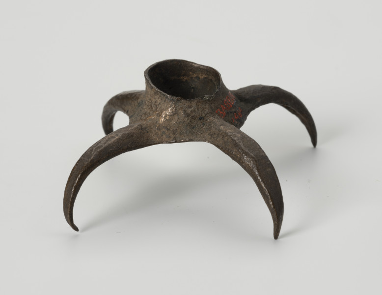 Pobocznica wędzidła końskiego (krępulec) - ujęcie z boku; Krępulec tzw. kolczasty złożony jest z niewielkiej tulejki zaopatrzonej w cztery kolczaste ramiona lekko zagięte do środka. Przedmiot wykonany jest z brązu.