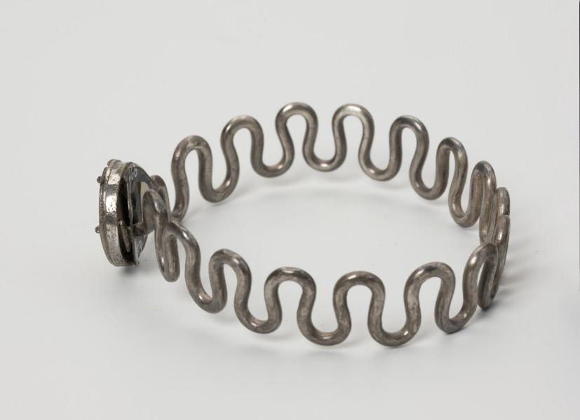 Bransoleta wężykowata - ujęcie z boku; Bransoleta srebrna wężykowata z okrągłym zapięciem kapsułkowym z lutowanej blachy. Kabłąk z kolei tworzy srebrny drut o średnicy 2 mm wygięty w gęsty esowaty zygzak.