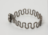 Bransoleta wężykowata - ujęcie z boku; Bransoleta srebrna wężykowata z okrągłym zapięciem kapsułkowym z lutowanej blachy. Kabłąk z kolei tworzy srebrny drut o średnicy 2 mm wygięty w gęsty esowaty zygzak.