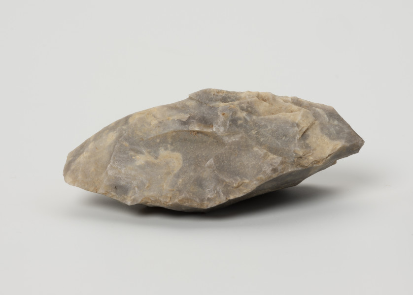 Ciosak - ujęcie z przodu; Niewielki ciosak o przekroju trójkątnym (płasko-wypukły) wykonany na masywnym odłupku, pierwotnie był nieco większy, co sugerują ślady napraw widoczne w okolicy części pracującej. Wyraźnie widoczne wyświecenia przy obuchu powstały na skutek oprawiania.