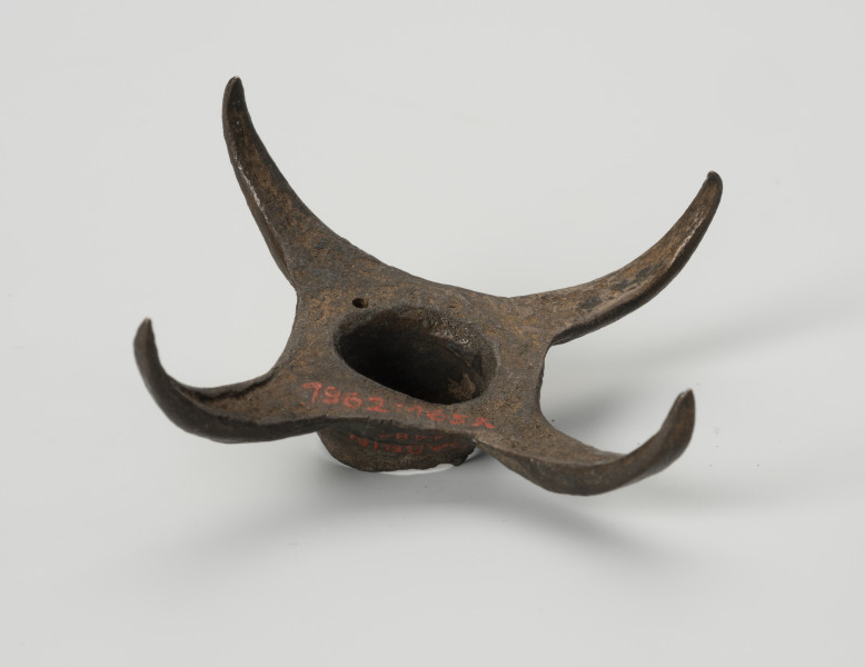 Pobocznica wędzidła końskiego (krępulec) - ujęcie z dołu; Krępulec tzw. kolczasty złożony jest z niewielkiej tulejki zaopatrzonej w cztery kolczaste ramiona lekko zagięte do środka. Przedmiot wykonany jest z brązu.