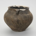 Waza typu IV (Wołągiewicz) - ujęcie z boku; Naczynie ceramiczne (waza) barwy ciemno brunatnej o chropowaconej części dolnej i wygładzanej górnej partii. Waza ma dwa przewężone ucha. Na brzuścu zdobiona chropowaconymi pasami w układzie podwójnego zygzaka. Wysokość wazy wynosi 19,8 cm, średnica brzuśca 22 cm, a średnica wylewu 21 cm.
