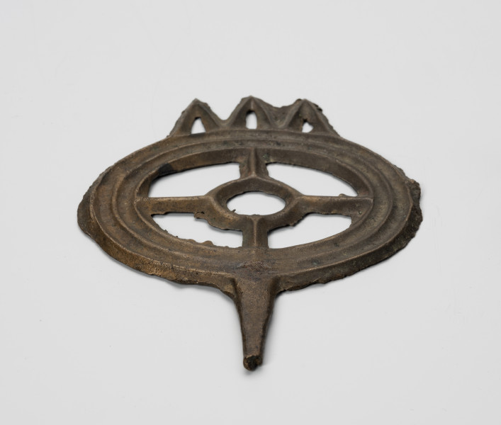 Szpila typu lüneburskiego z główką w kształcie koła szprychowego - ujęcie z przodu; Jest to szpila z brązu o okazałej kolistej główce w formie tzw. koła szprychowego - tzn. w zewnętrzy, szeroki profilowany okrąg (profilowanie stanowi imitacje trzech współśrodkowych okręgów) wpisany jest mniejszy okrąg, połączony czterema 