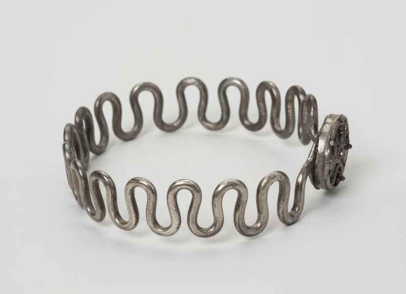 Bransoleta wężykowata - ujęcie z boku; Bransoleta srebrna wężykowata z okrągłym zapięciem kapsułkowym z lutowanej blachy. Kabłąk z kolei tworzy srebrny drut o średnicy 2 mm wygięty w gęsty esowaty zygzak.